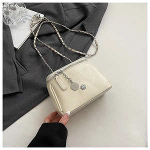Close-up of cream leather crossbody bag with chain strap and camellia charm decoration