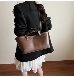 Detail of a dark brown matte leather bucket bag with top handles and a minimalist button