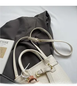 Detail of white lychee leather handbag with gold hardware and beaded bear charm