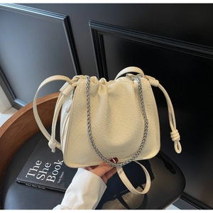 Detail view of cream white croc-textured bucket bag with drawstring and silver chain strap
