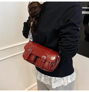 Detail of dark red glossy patent leather underarm bag with retro buckles and lace strap
