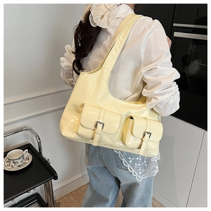 Detail of creamy yellow patent leather shoulder bag with two metal buckle pockets