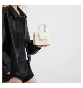 Detail of a creamy white mini handbag featuring matte leather and metal side buckles