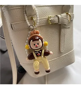 Detail of cartoon girl doll bag charm with pearl strap on cream bucket handbag