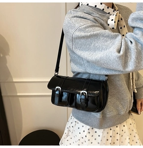 Detail of black glossy shoulder bag with dual front pockets and silver metal buckles