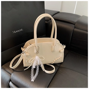 Détail du sac Boston crème avec surpiqûres et accessoire nœud en dentelle et perles