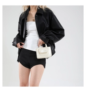 Chic model wearing a black oversized leather jacket with a mini white patent leather bag