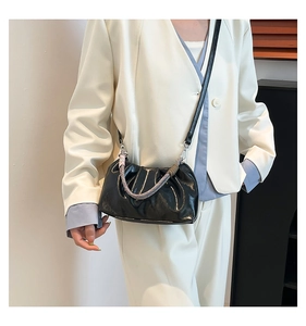 Detail of black pleated cloud bag with braided handle and leather strap on beige suit