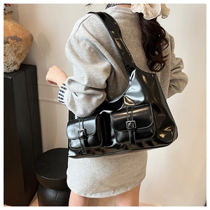 Detail view of black patent leather shoulder bag with vintage buckles on a model