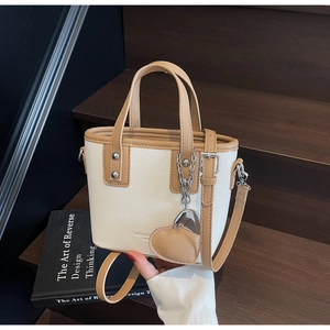 Detail of cream bucket bag with brown trim and heart charm on a wooden stair