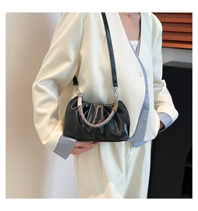 Close-up of black ruched cloud bag with woven ring handle and leather strap on blazer