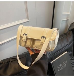 Close-up of cream white shoulder bag featuring double front buckle pockets and silver hardware