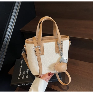 Detail of a two-tone bucket bag with litchi grain leather and heart pendant