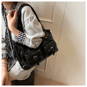 Macro detail of glossy black tote bag featuring double pockets with silver metal buckles