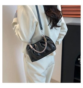 Detail of black pleated cloud bag with colorful woven handle and sleek leather surface