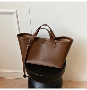 Detail of dark brown leather bucket bag with top handles and adjustable strap on stand