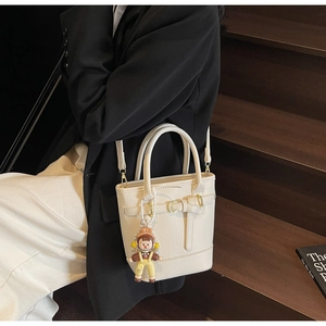 Detail of cream lychee texture bucket bag with leather buckle and cartoon charm on model