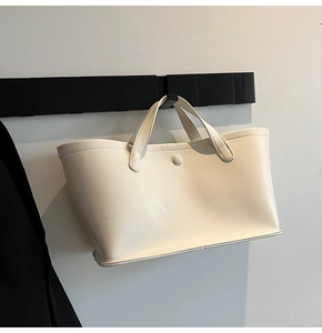 Detail view of cream faux leather tote bag hanging with snap button closure and sturdy handles