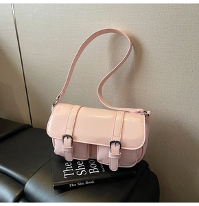 Close-up of light pink baguette shoulder bag with metal buckles on a fashion book