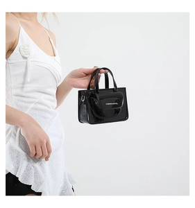 Close-up of black patent leather mini square handbag with top handle and metallic D-ring detail