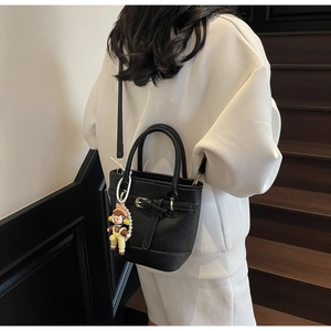 Detail of black textured leather bucket bag with gold buckle and cute pearl monkey charm