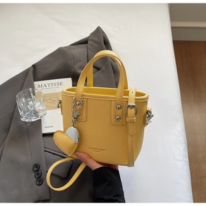 Detail view of ginger yellow leather bucket bag with silver studs and heart-shaped charm
