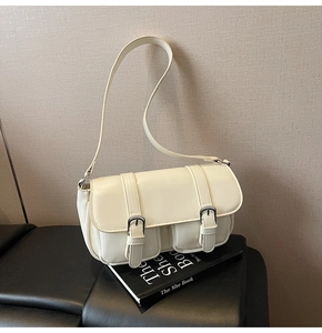 Detail of cream white faux leather shoulder bag with decorative straps and twin pockets