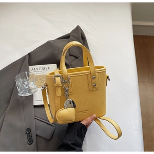 Detail of yellow lychee leather bucket bag with heart pendant and silver metal chain strap