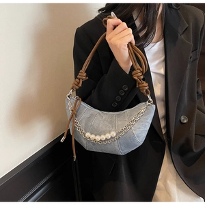 Détail du sac croissant en jean bleu clair avec anse en cuir torsadé et perles