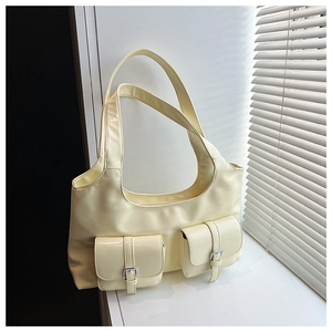 Detail of cream leather hobo bag with dual pockets and silver buckles in sunlight