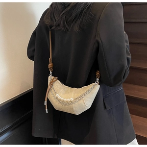 Détail du sac croissant beige avec chaîne argentée et bandoulière à nœud sur blazer