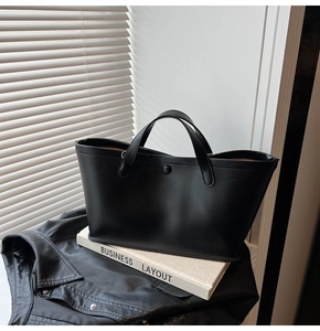 Detail of a minimalist black leather tote bag with matte texture and snap closure design