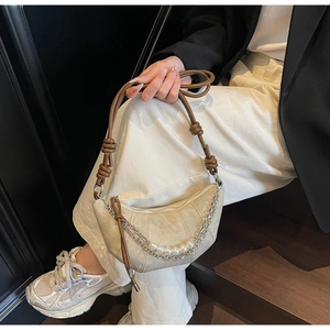 Détail du sac croissant beige avec chaînes argentées, perles blanches et bandoulière à nœuds