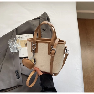 Detail of elegant cream and brown bucket bag placed on a grey blazer with stylish props