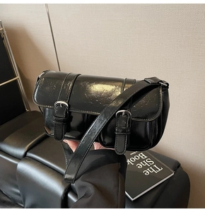 Close-up of black glossy patent leather crossbody bag with buckle straps on a leather sofa