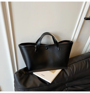 Detailed view of black matte leather tote bag with snap button on minimalist sofa