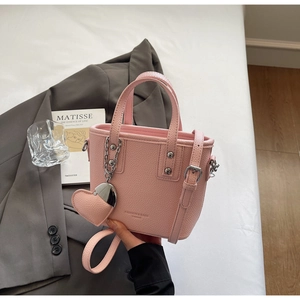 Detail of pink bucket bag with litchi texture leather, metal studs and heart pendant