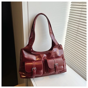 Close-up of a glossy burgundy shoulder bag with functional silver buckle pockets