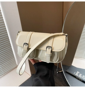 Close-up of cream leather shoulder bag with parallel buckle straps and side pocket details