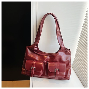 Detail of dark red high-gloss tote bag with dual pockets and metal buckle accents
