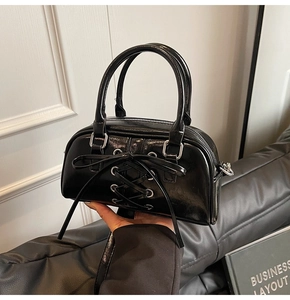 Dettaglio borsa Boston in vernice nera con fiocco intrecciato e occhielli argentati