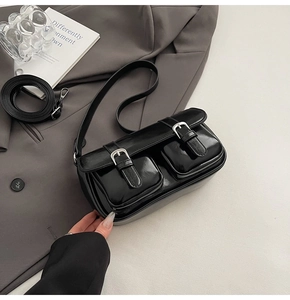 Detail of glossy black patent leather bag with silver buckles on a gray suit jacket
