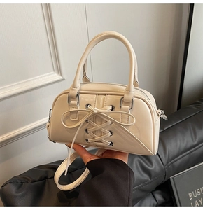 Dettaglio della borsa a bauletto crema con fiocco decorativo e occhielli argentati