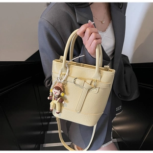 Detail of light yellow lychee grain bucket bag with pearl chain and doll charm