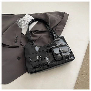 Detail of black patent leather tote bag featuring two front pockets and metal buckles