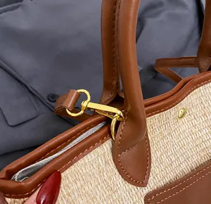 Close-up of golden metal lobster clasp and brown leather trim on a woven tote bag