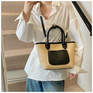 Detail of woven straw tote bag featuring black leather pocket and handles on stairs