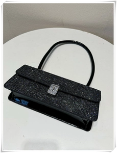 Close-up of black rhinestone shoulder bag with shiny patent leather base and crystal buckle