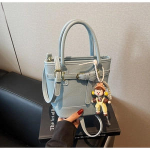 Close-up of light blue lychee pattern bucket bag with decorative buckle and doll charm