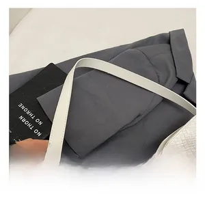 Close-up of white woven tote bag with a wide shoulder strap on a grey suit jacket